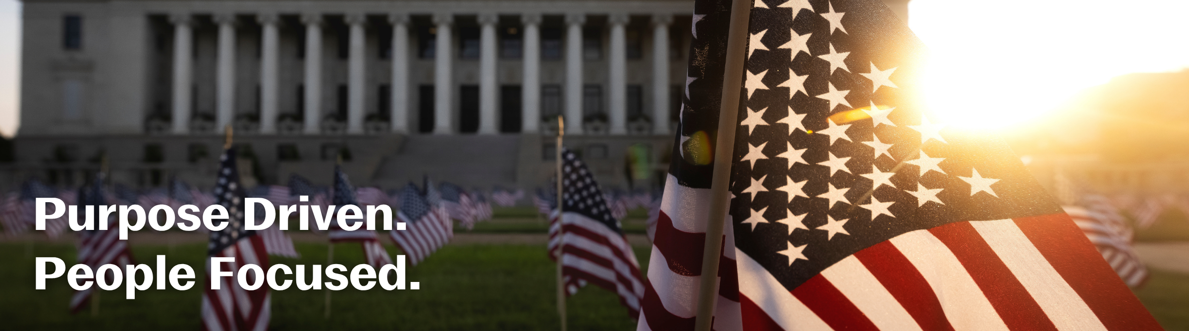 Administration Building with flags in the lawn. Text: Purpose Driven. People Focused.